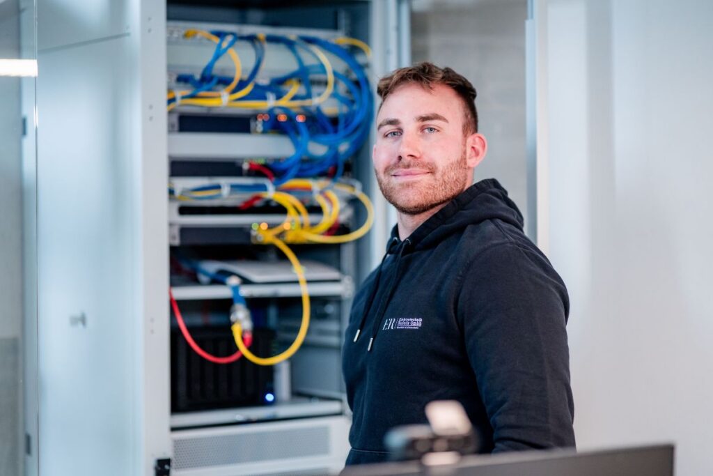 Moritz Rulofs steht vor geöffnetem Schaltschrank in der Werkstatt